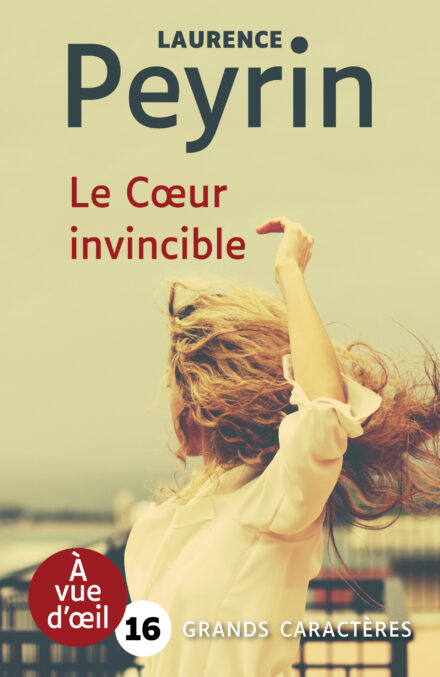 Couverture du livre Le Cœur invincible de Laurence Peyrin en grands caractères (police 16). Une femme aux cheveux blonds ondulés, de dos, lève les bras dans un mouvement fluide au bord d’un quai ou d’une rambarde.