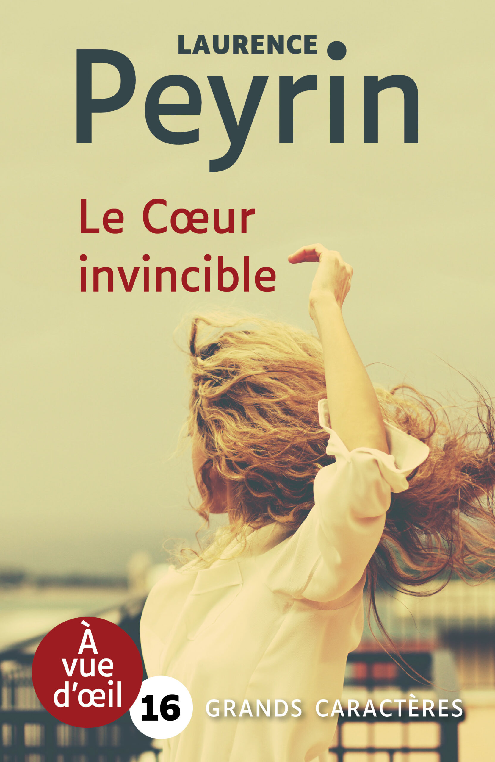 Couverture du livre Le Cœur invincible de Laurence Peyrin en grands caractères (police 16). Une femme aux cheveux blonds ondulés, de dos, lève les bras dans un mouvement fluide au bord d’un quai ou d’une rambarde.
