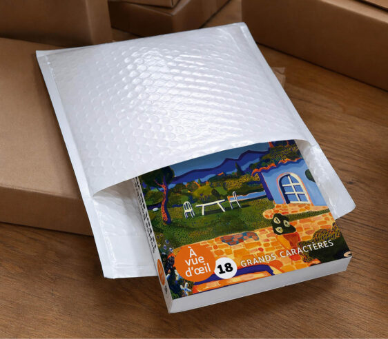 Livre en grands caractères partiellement glissé dans une enveloppe de protection blanche, prêt à être expédié.